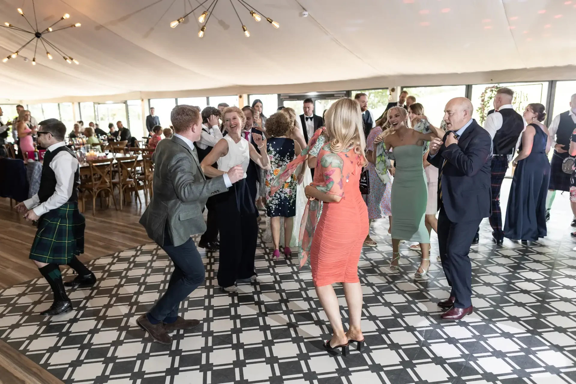 Guests dancing joyfully at a wedding reception under a tent with a black and white checkered dance floor.