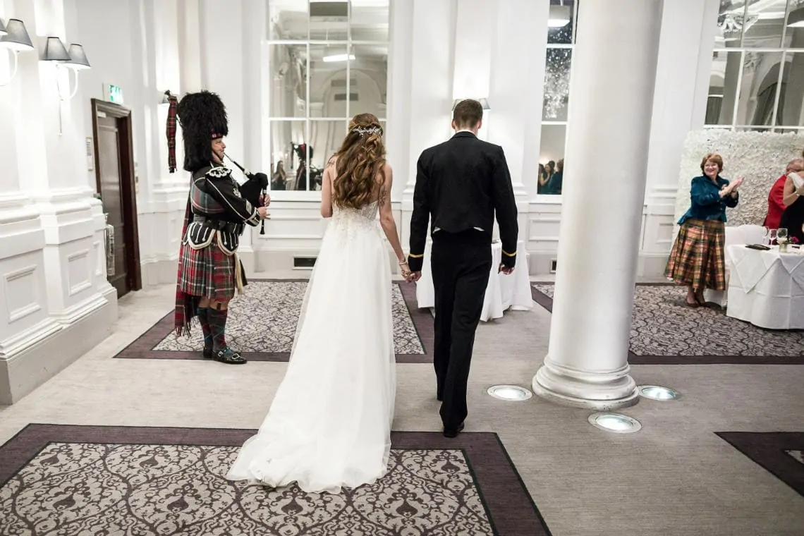 newlyweds are led by the piper into the King's Hall