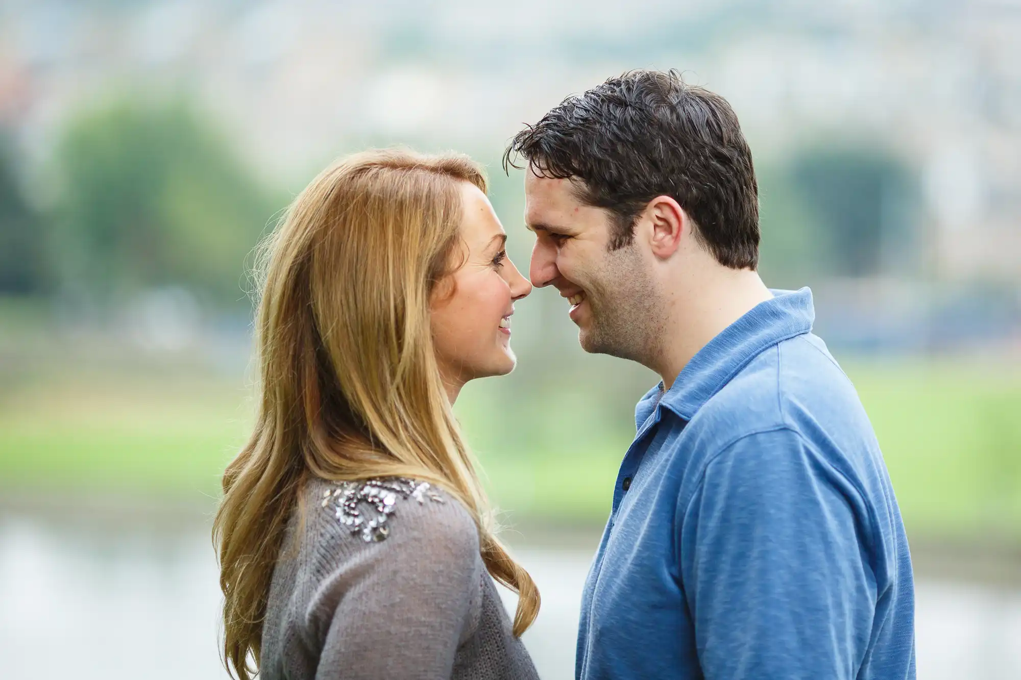 A couple standing close together, affectionately pressing their foreheads together, smiling gently with a blurred natural background.