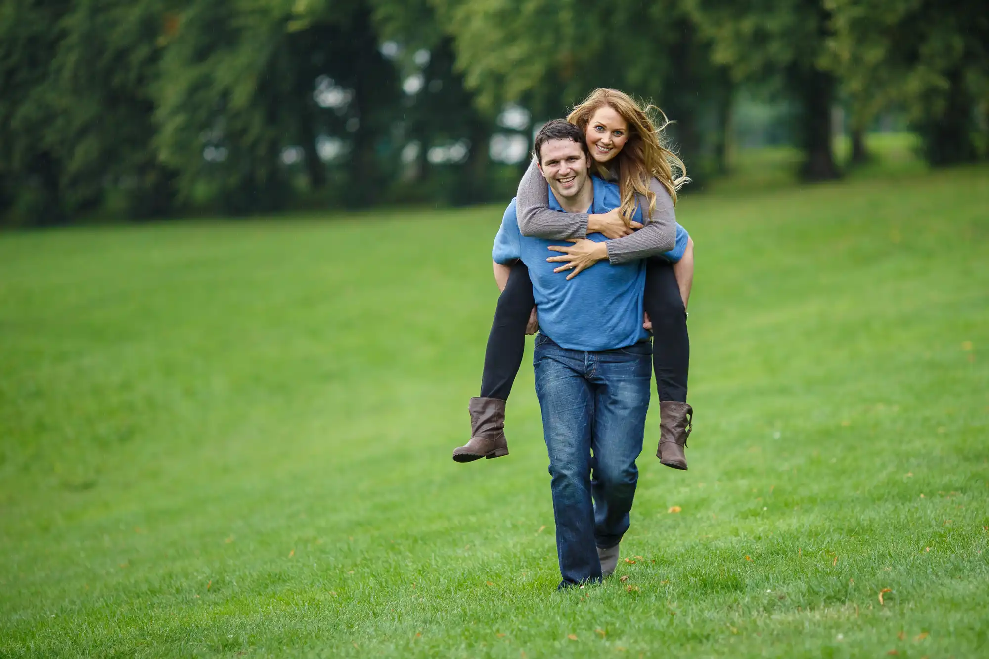 A man giving a woman a piggyback ride, both smiling, in a lush green park.