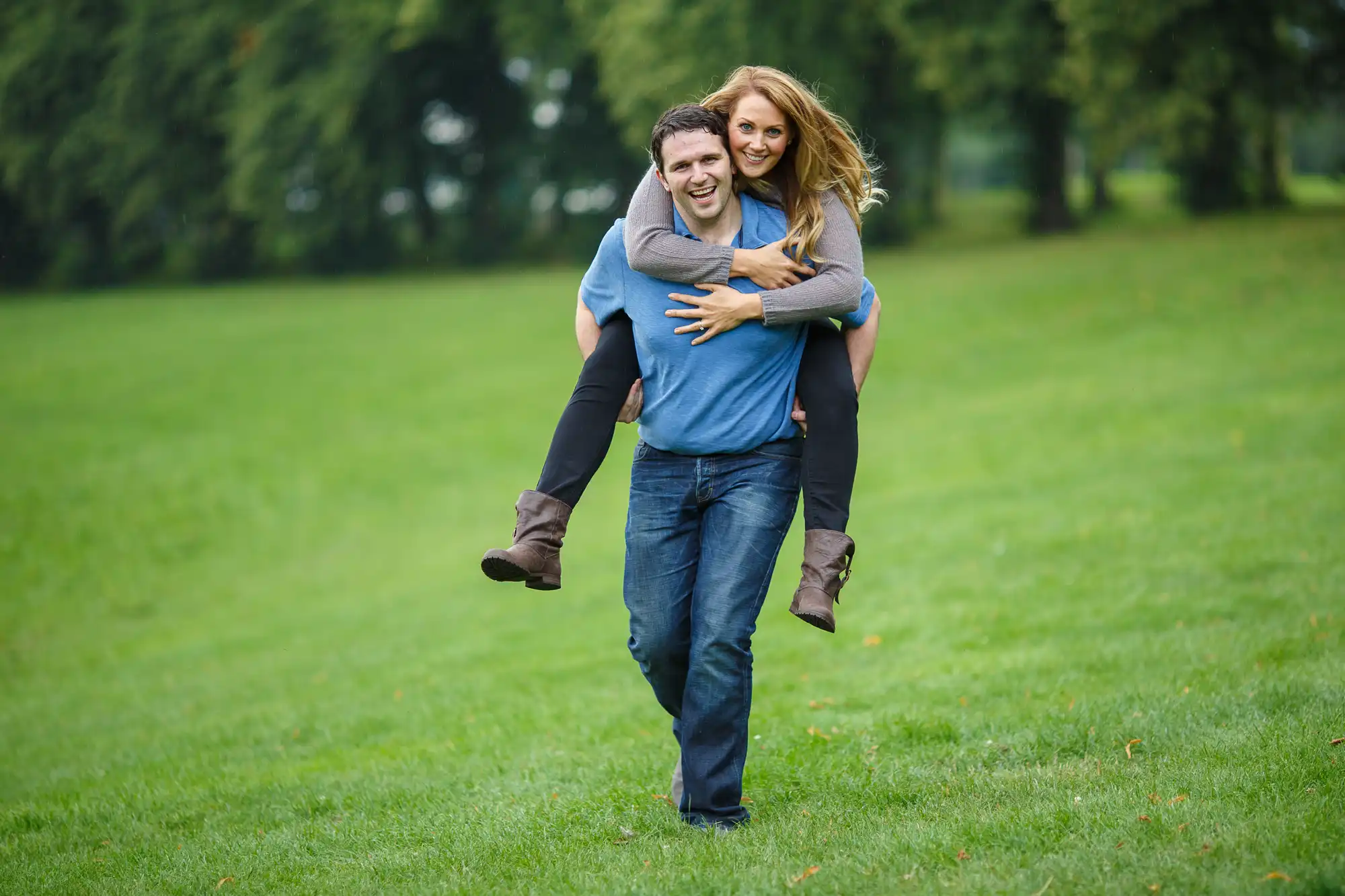 A man carrying a woman on his back, both smiling, in a lush green park.