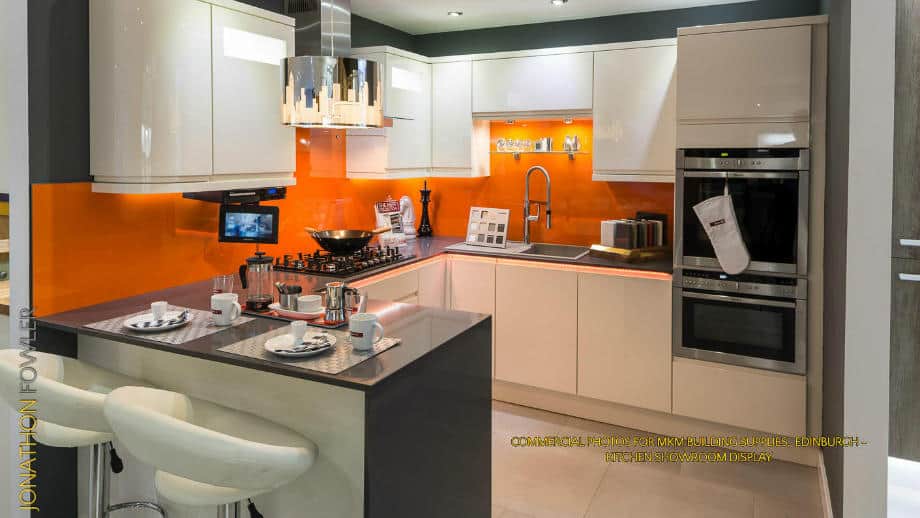 Modern kitchen interior with orange walls, white cabinets, and built-in stainless steel appliances. .