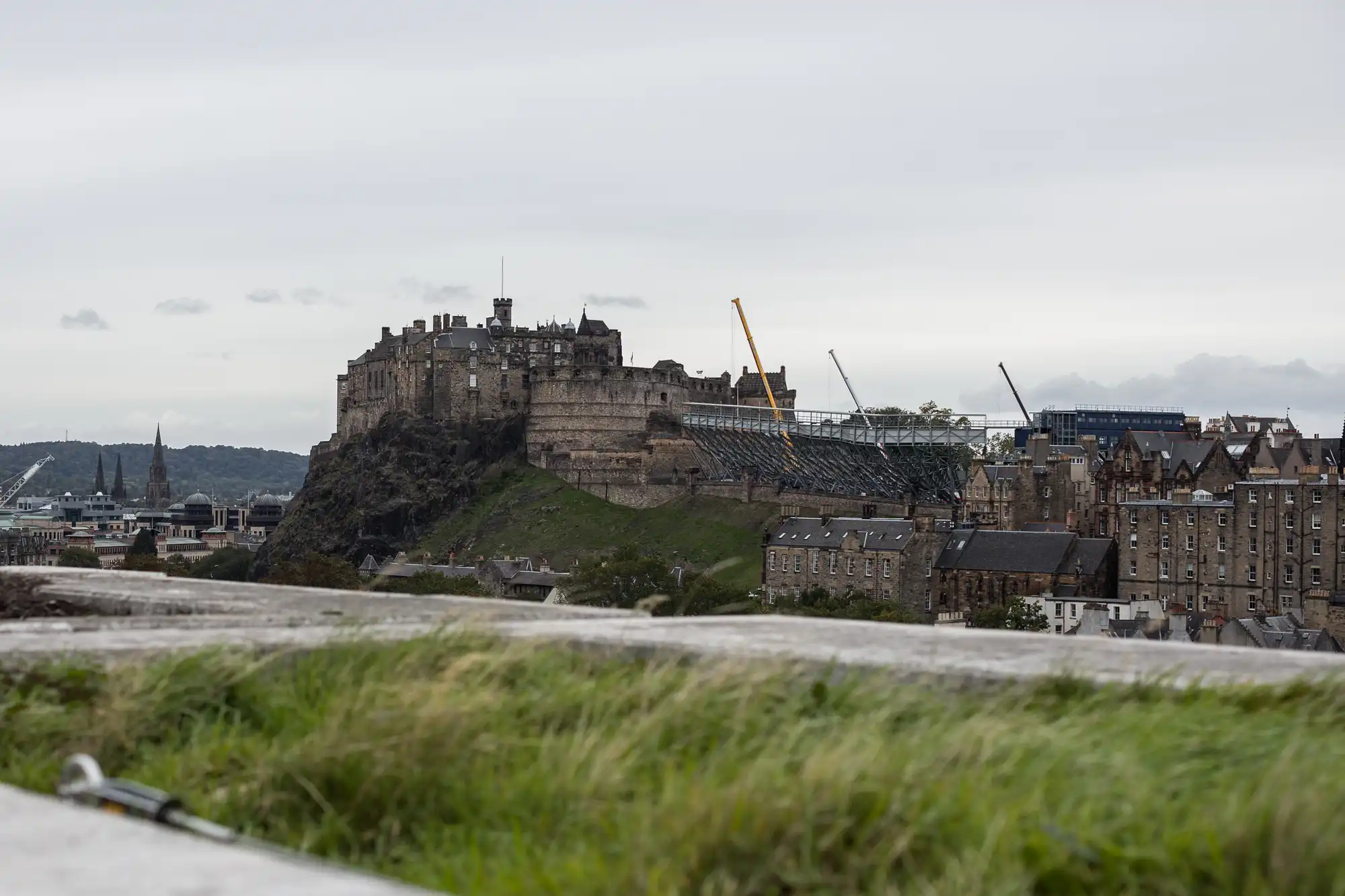 View of edinburgh castle on a cloudy day, with surrounding buildings and construction cranes visible.