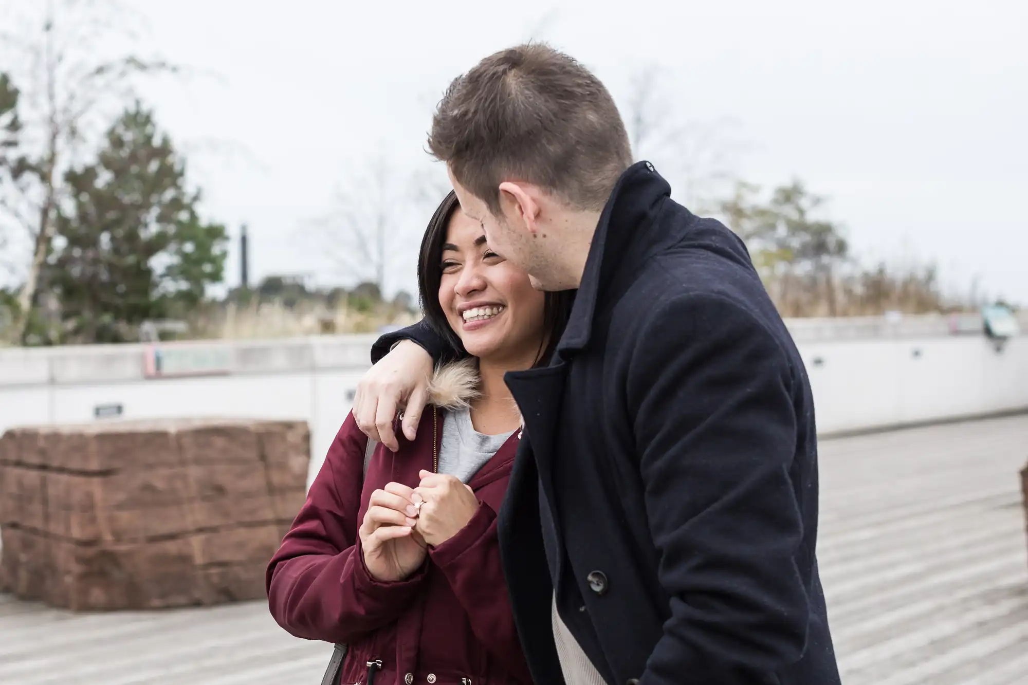 A couple smiling and embracing on a wooden deck, with the man kissing the woman's forehead.