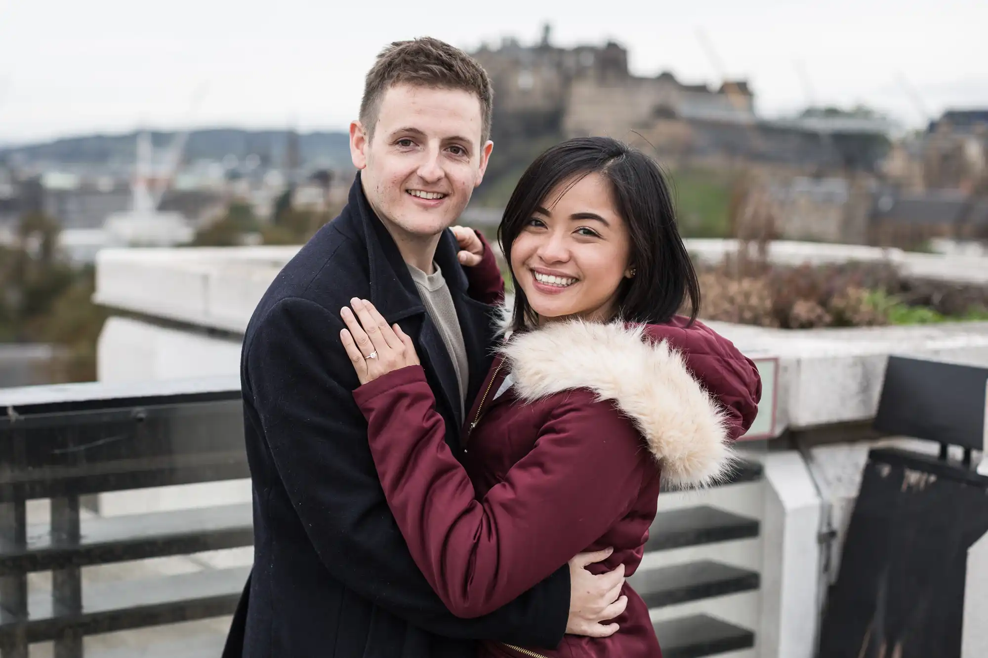A smiling couple embracing on a rooftop with a castle visible in the background.