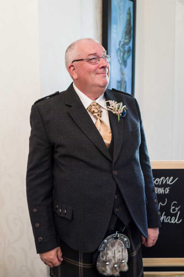 father of the bride waits while bride walks down the staircase