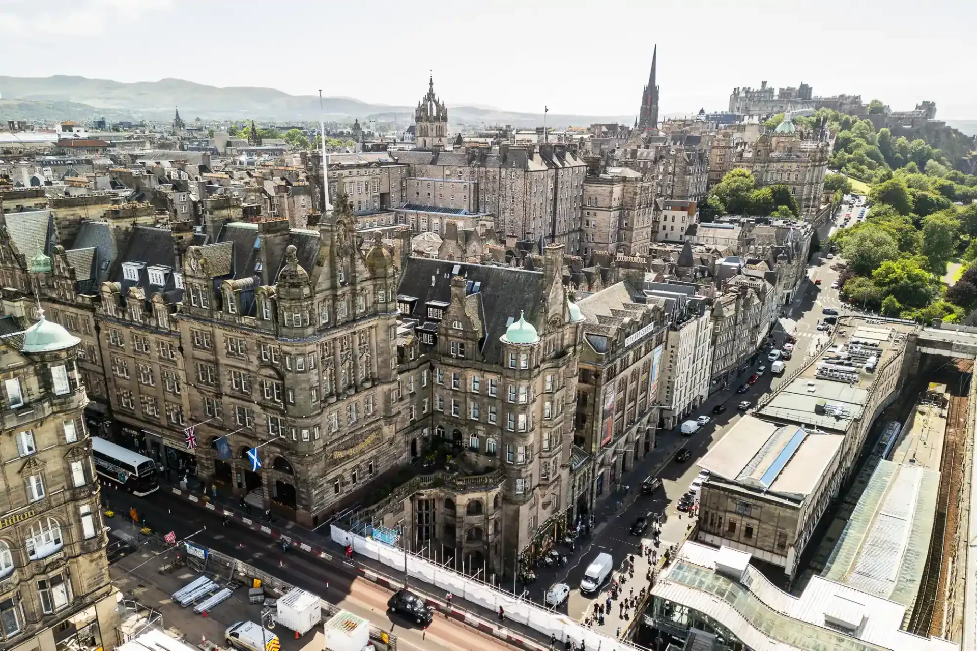 Aerial view of historic stone buildings and busy streets in central Edinburgh, Scotland, with The Scotsman Hotel visible in the foreground and Edinburgh Castle visible in the background.
