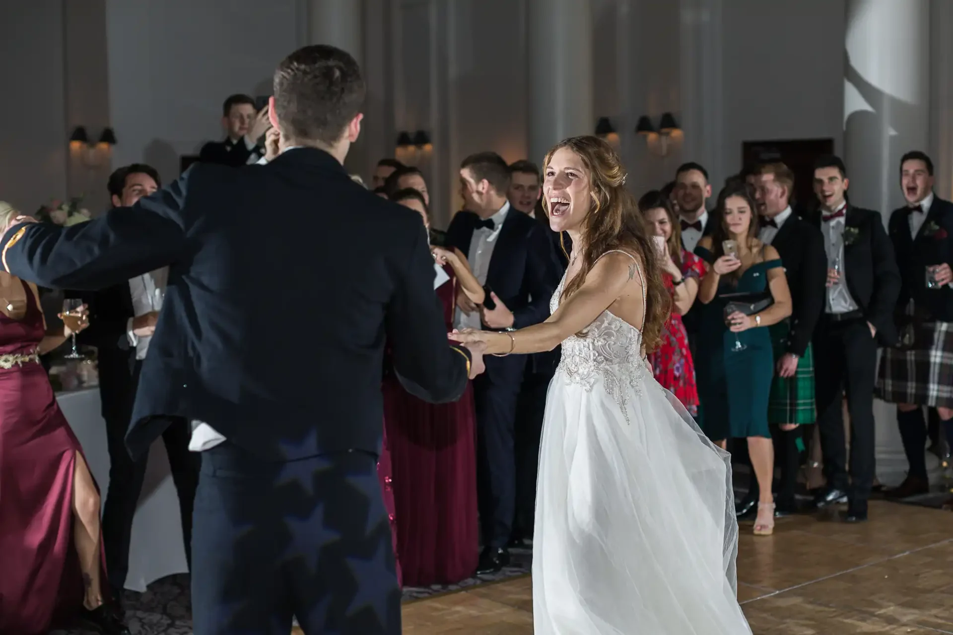 A bride and groom dance together while guests watch and smile at a formal indoor wedding reception at The George Hotel, Edinburgh.