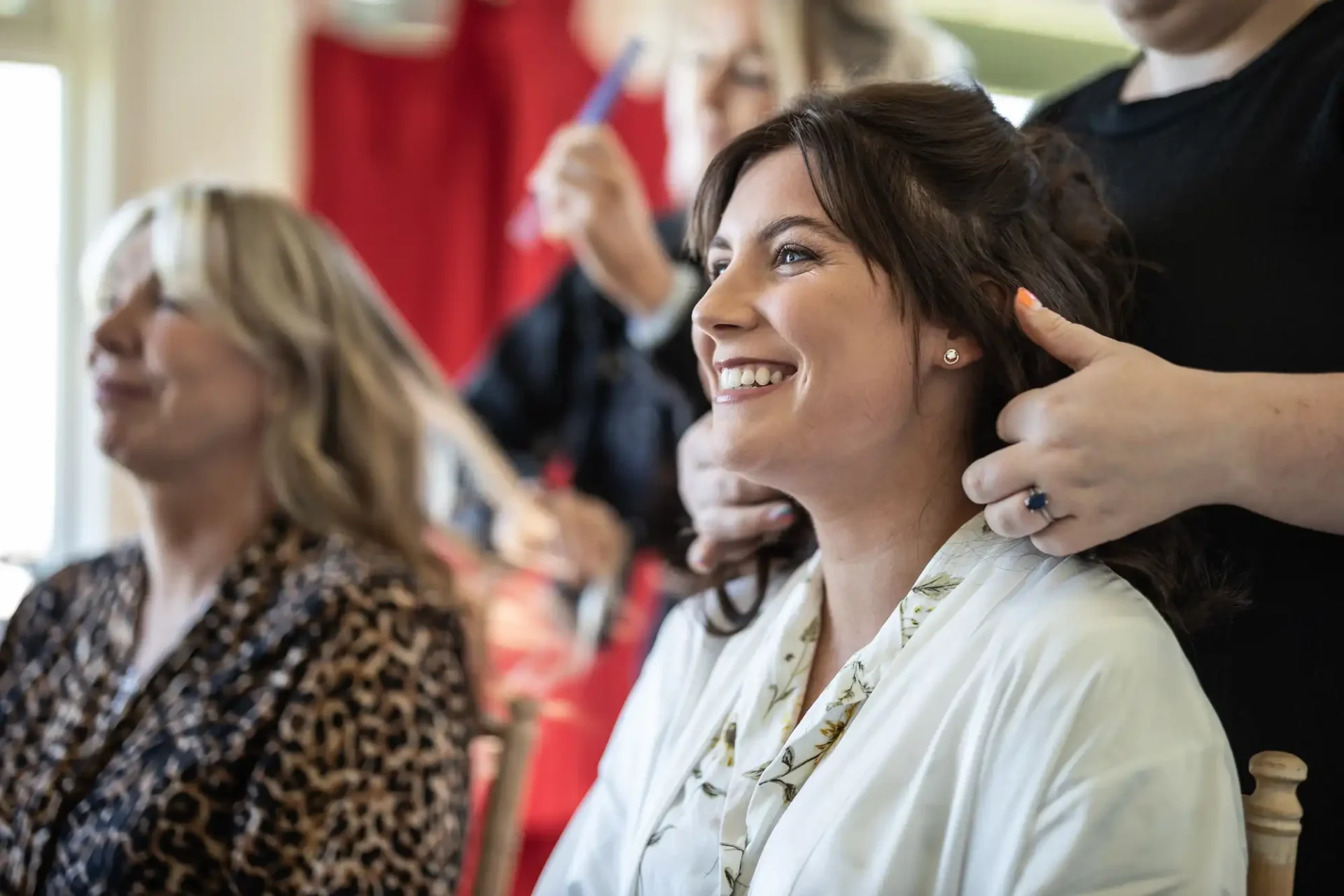 Two women getting their hair styled. One is smiling while another person styles her hair.