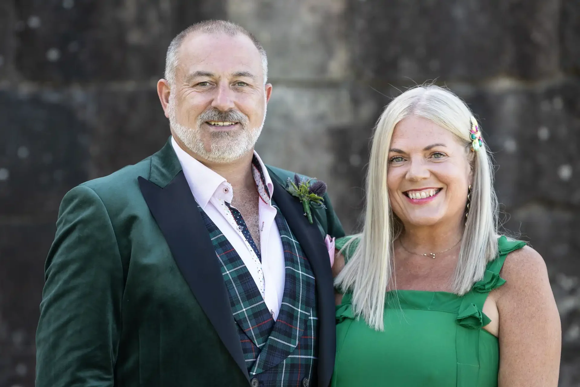 A man in a green suit and a woman in a green dress smile outdoors.