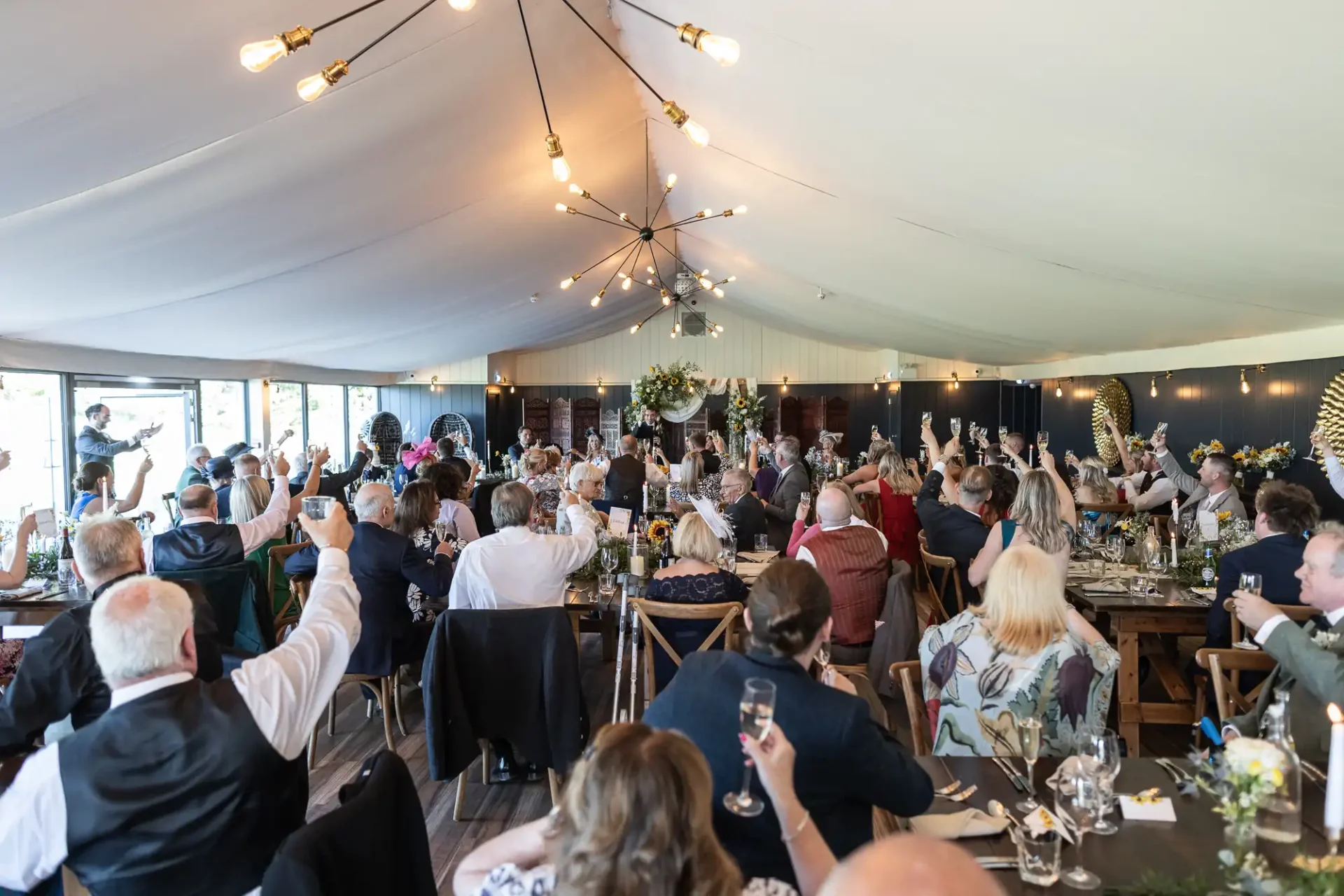 Guests raising glasses in a toast at a wedding reception inside a decorated tent.