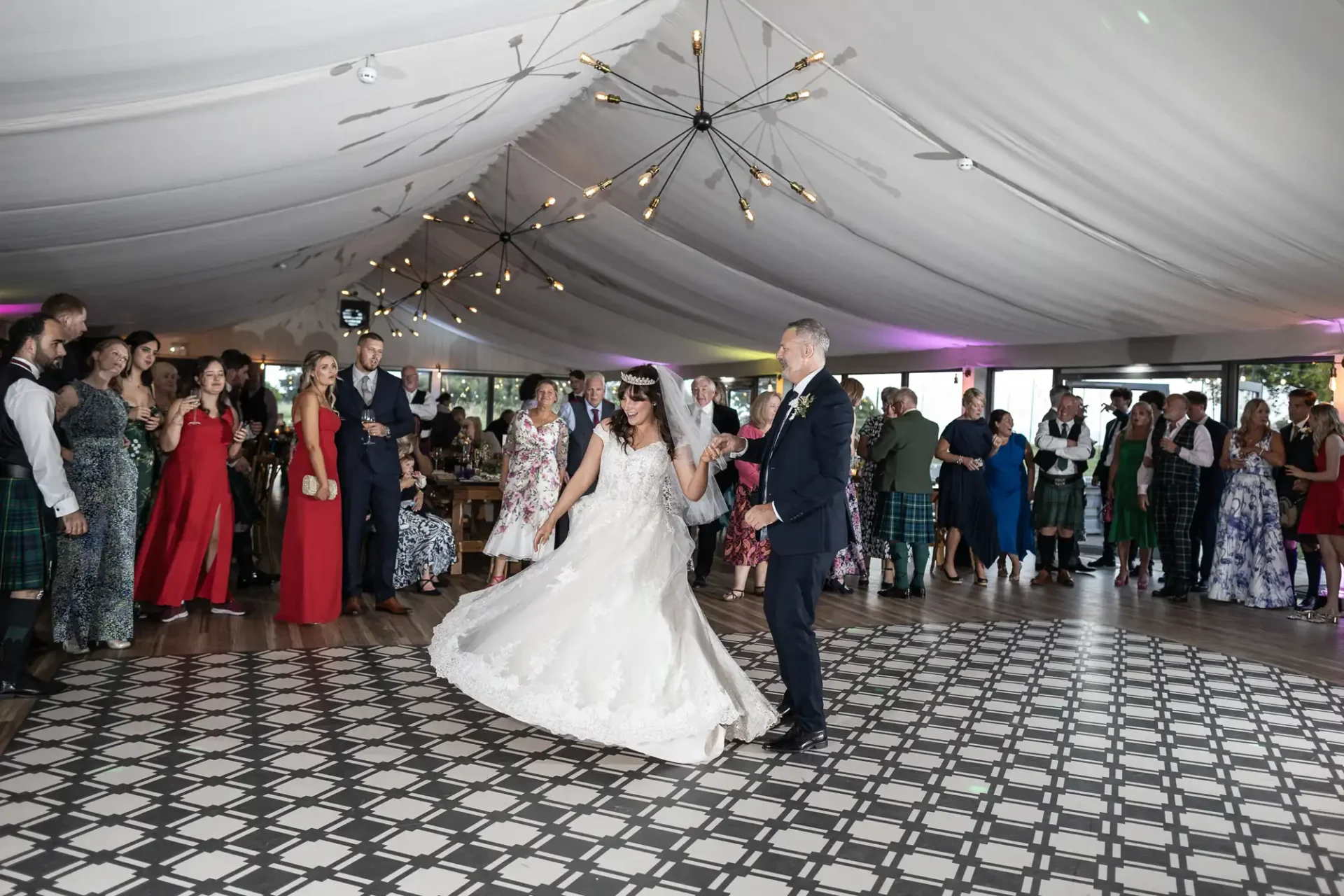 Bride and groom dancing under a tented ceiling with guests in the background.