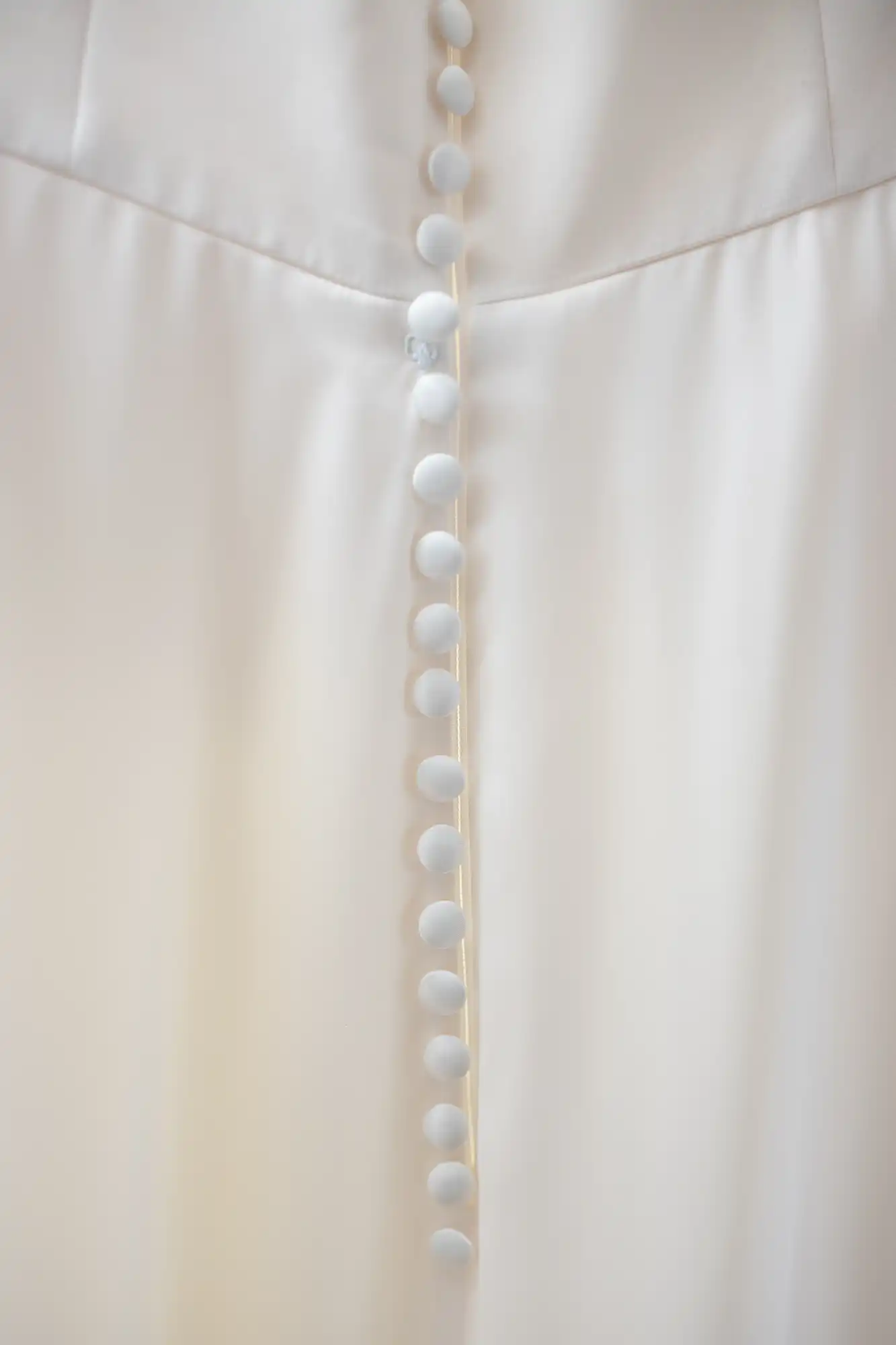 Close-up of a row of white buttons on a white fabric, possibly part of a garment.