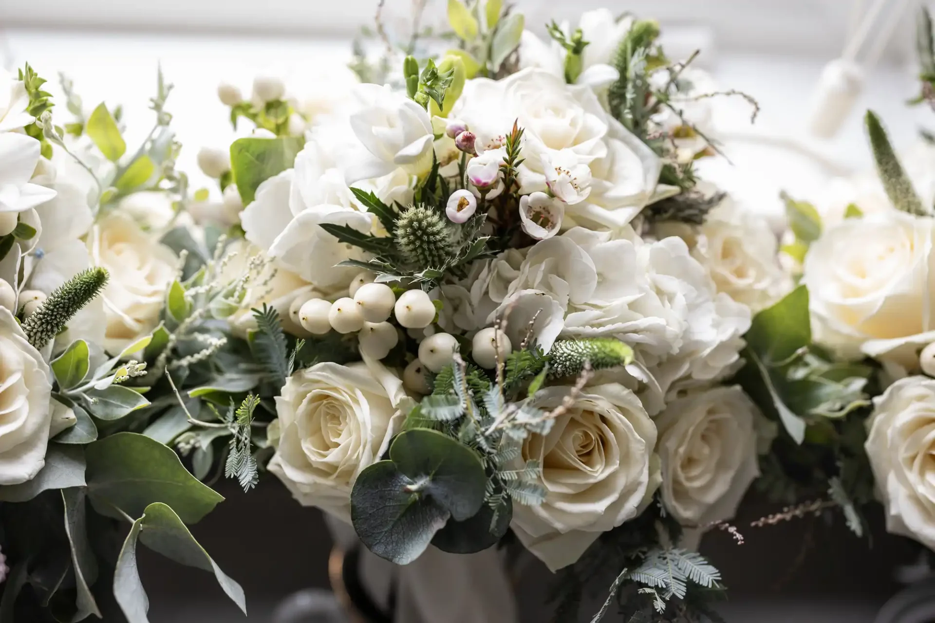 A bouquet of white roses, eucalyptus leaves, and other greenery with small white berries.