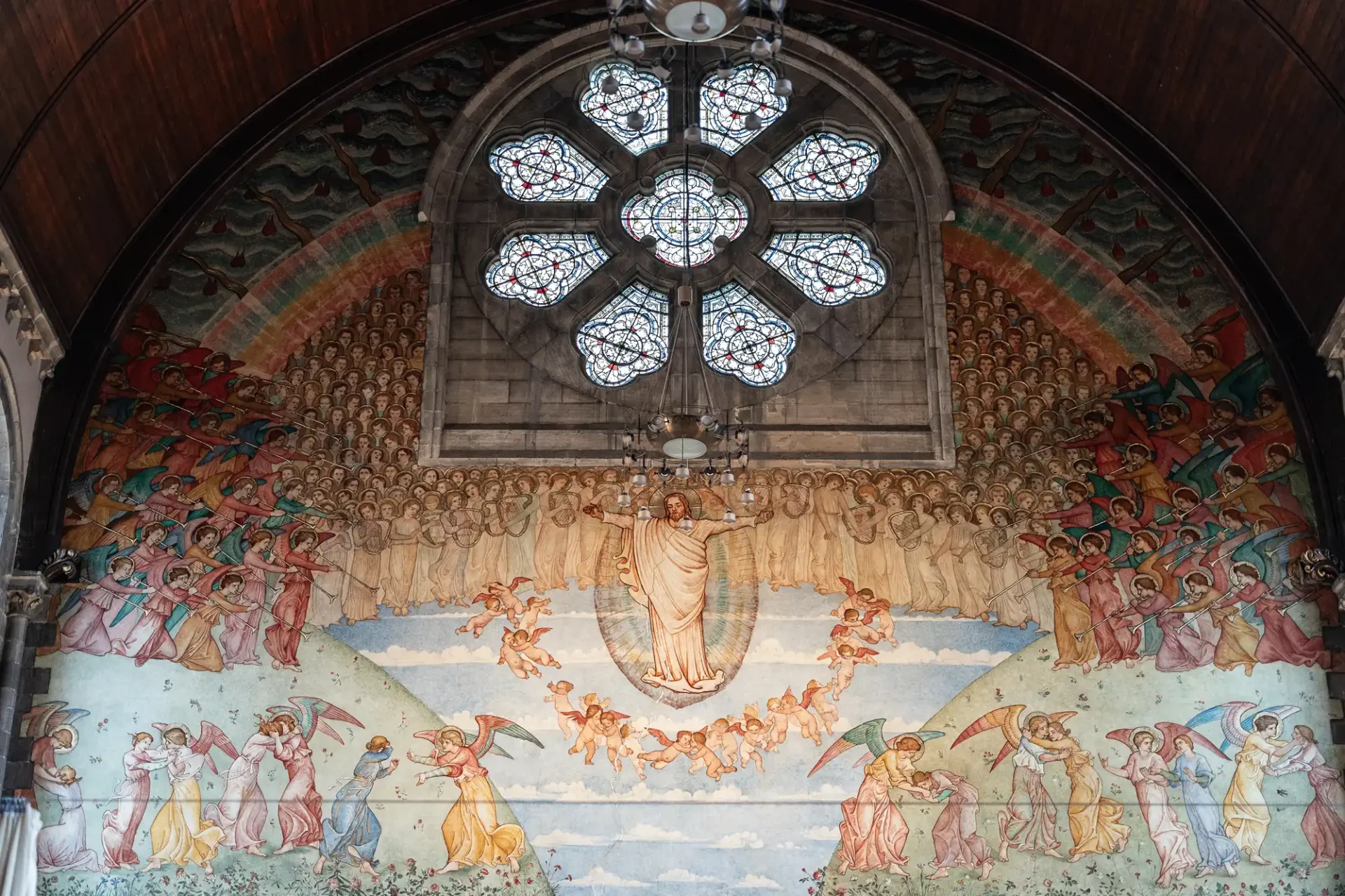 A mural depicts an ascension scene with a central figure in white, surrounded by angels and figures, beneath a large stained glass window in a church's arched ceiling.