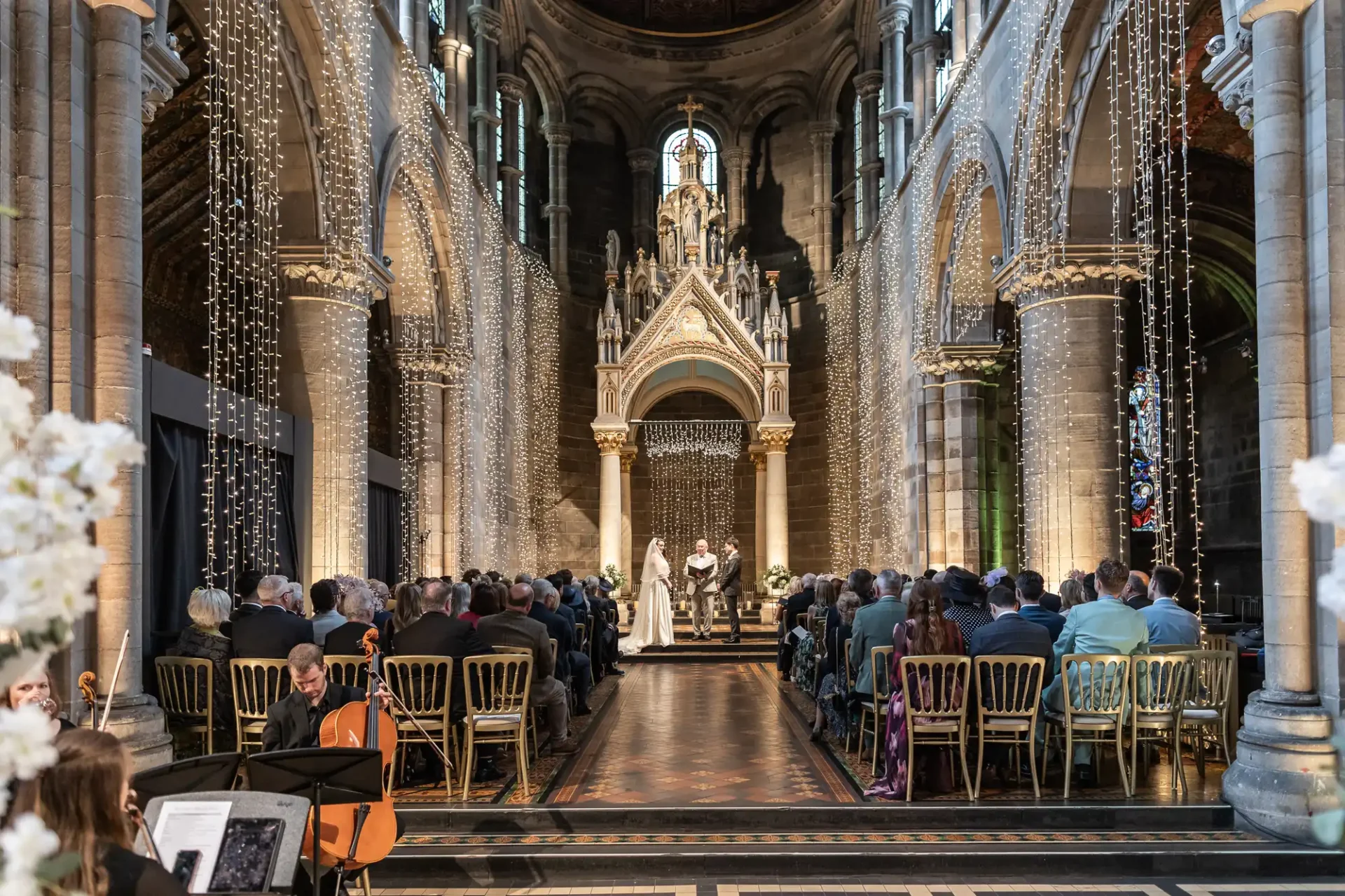 A couple stands at the altar in a grand church during a wedding ceremony, with guests seated on either side of the aisle.