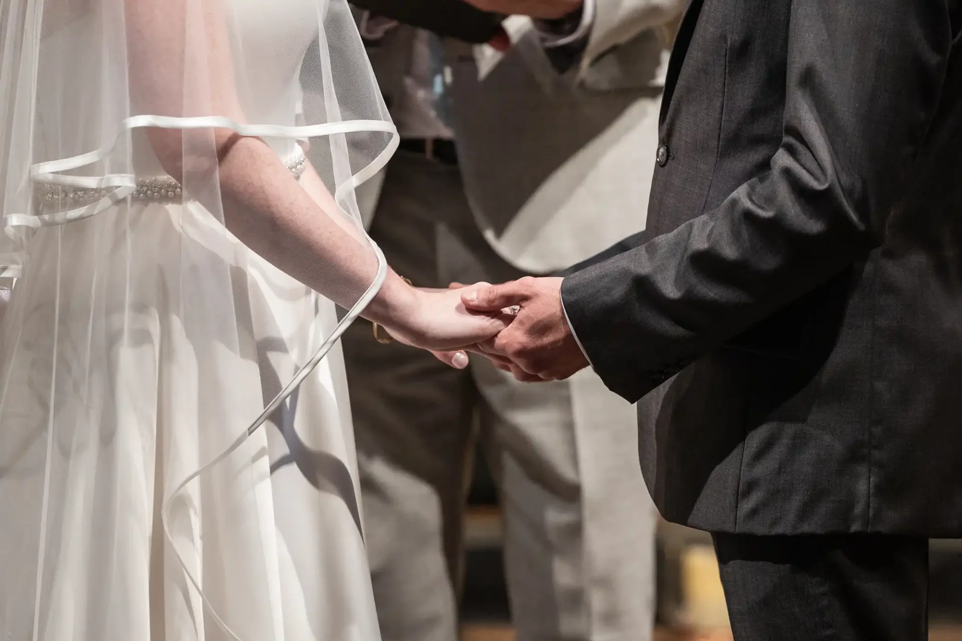 A bride and groom hold hands during a wedding ceremony, standing side by side.