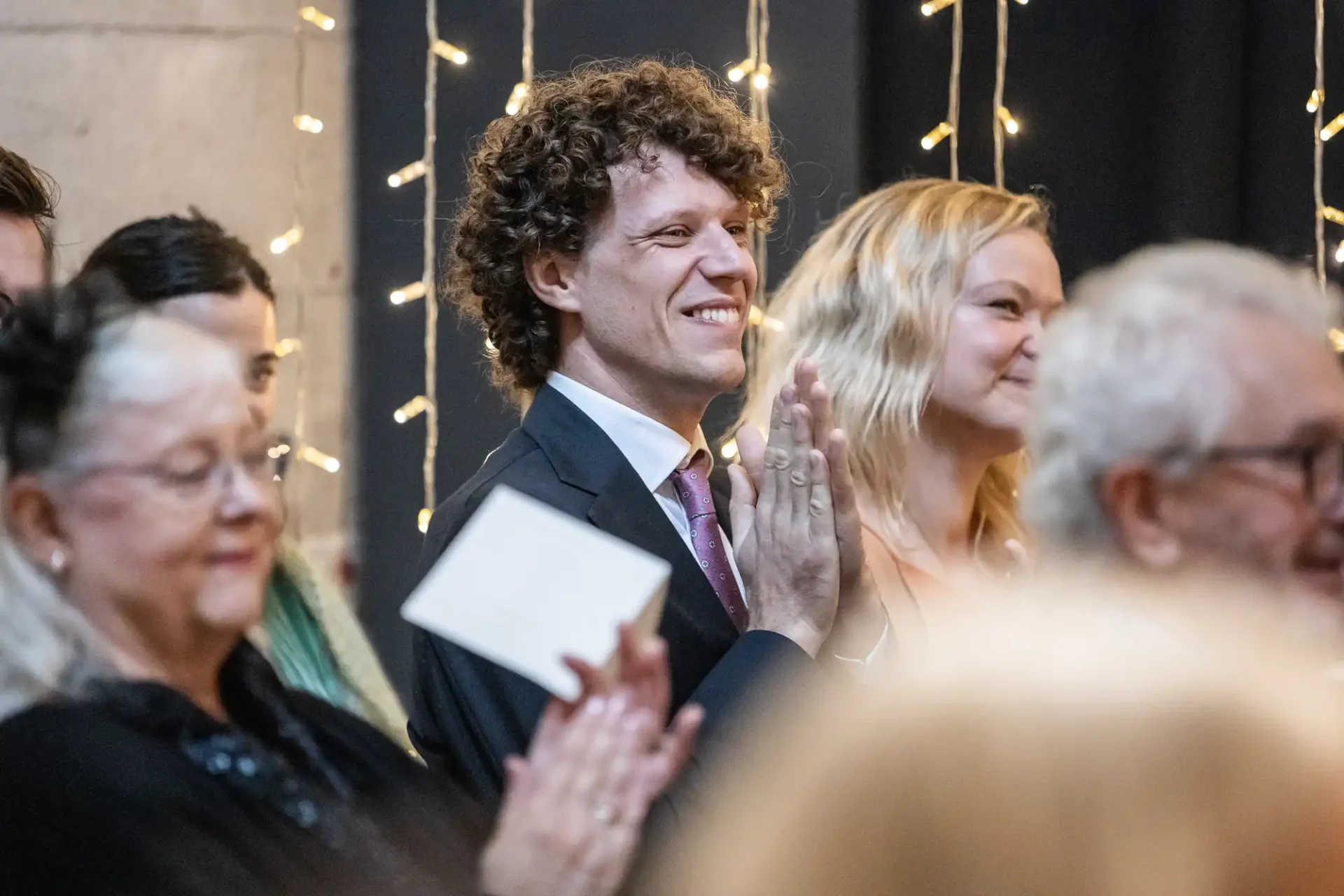 People clapping at an event, with string lights in the background.