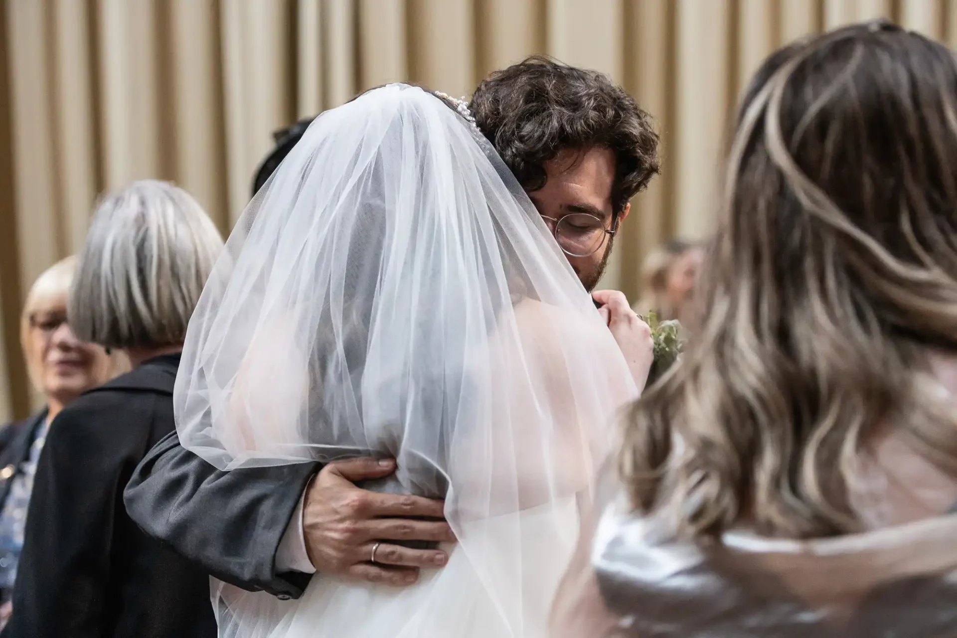 Bride and groom embracing in a warm hug during their wedding ceremony, surrounded by guests.