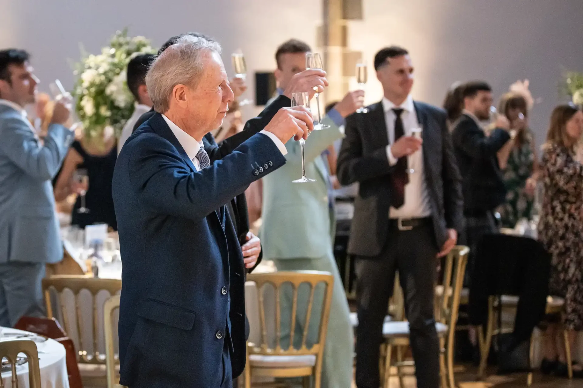 A group of people in formal attire stand and raise champagne glasses in a toast at an event.