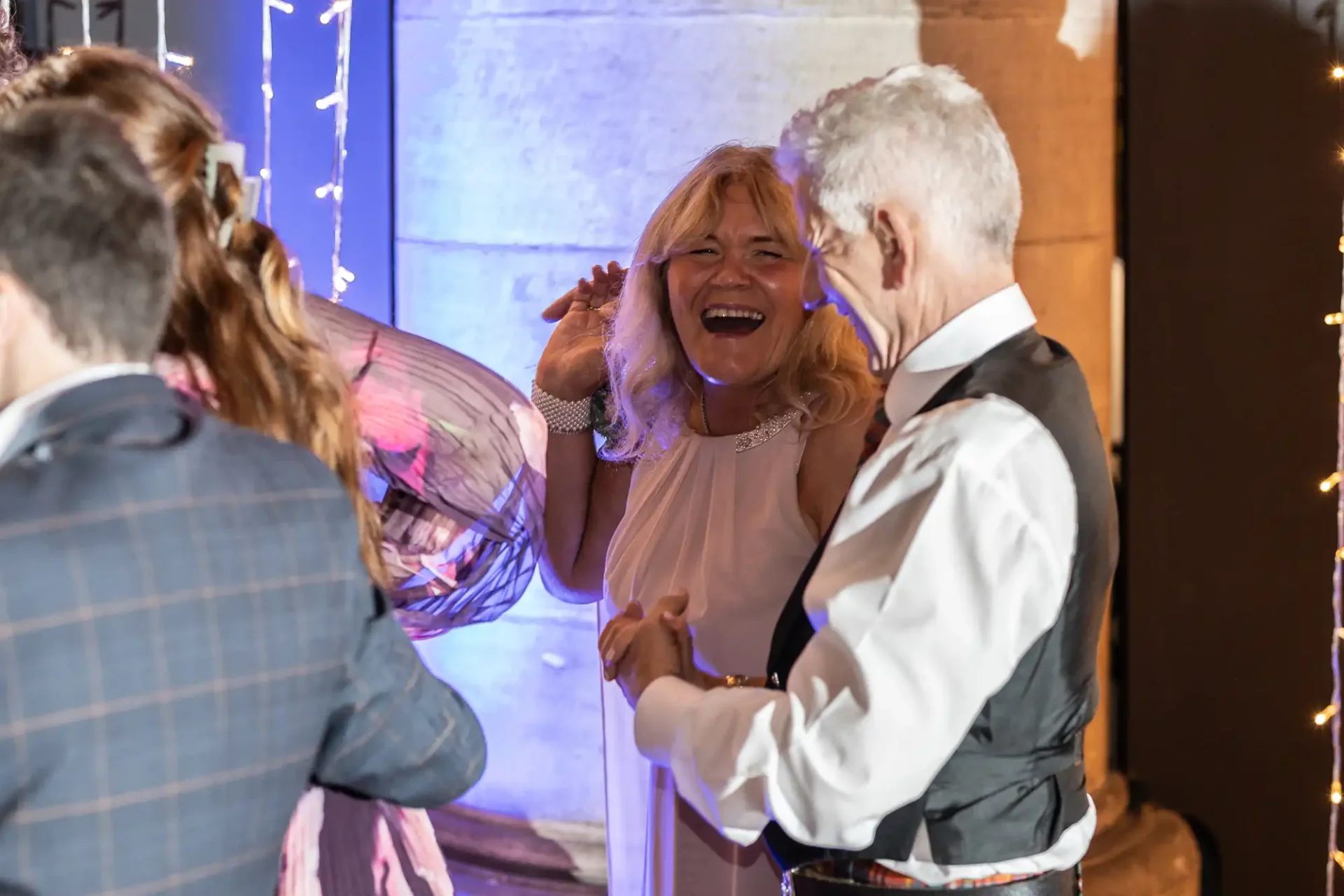 People laughing and talking at an indoor event with decorative lights and a column in the background.